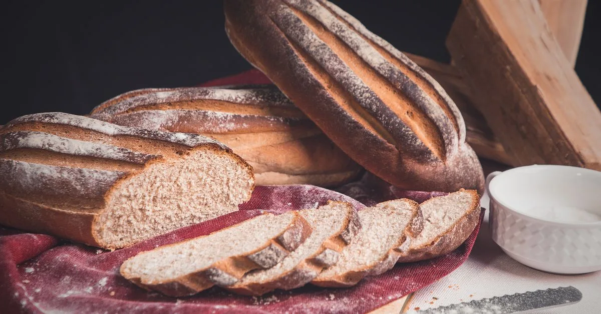 Angeschnittene Roggenbrotlaibe auf einem Tuch, daneben Mehl in einer Schale